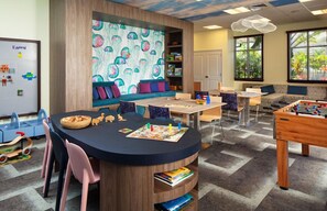 Ein Kinderspielzimmer mit einem runden Tisch, Stühlen, einer Couch und einem Kicker.