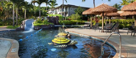 A pool area with a water feature, lounge chairs, and palm trees.