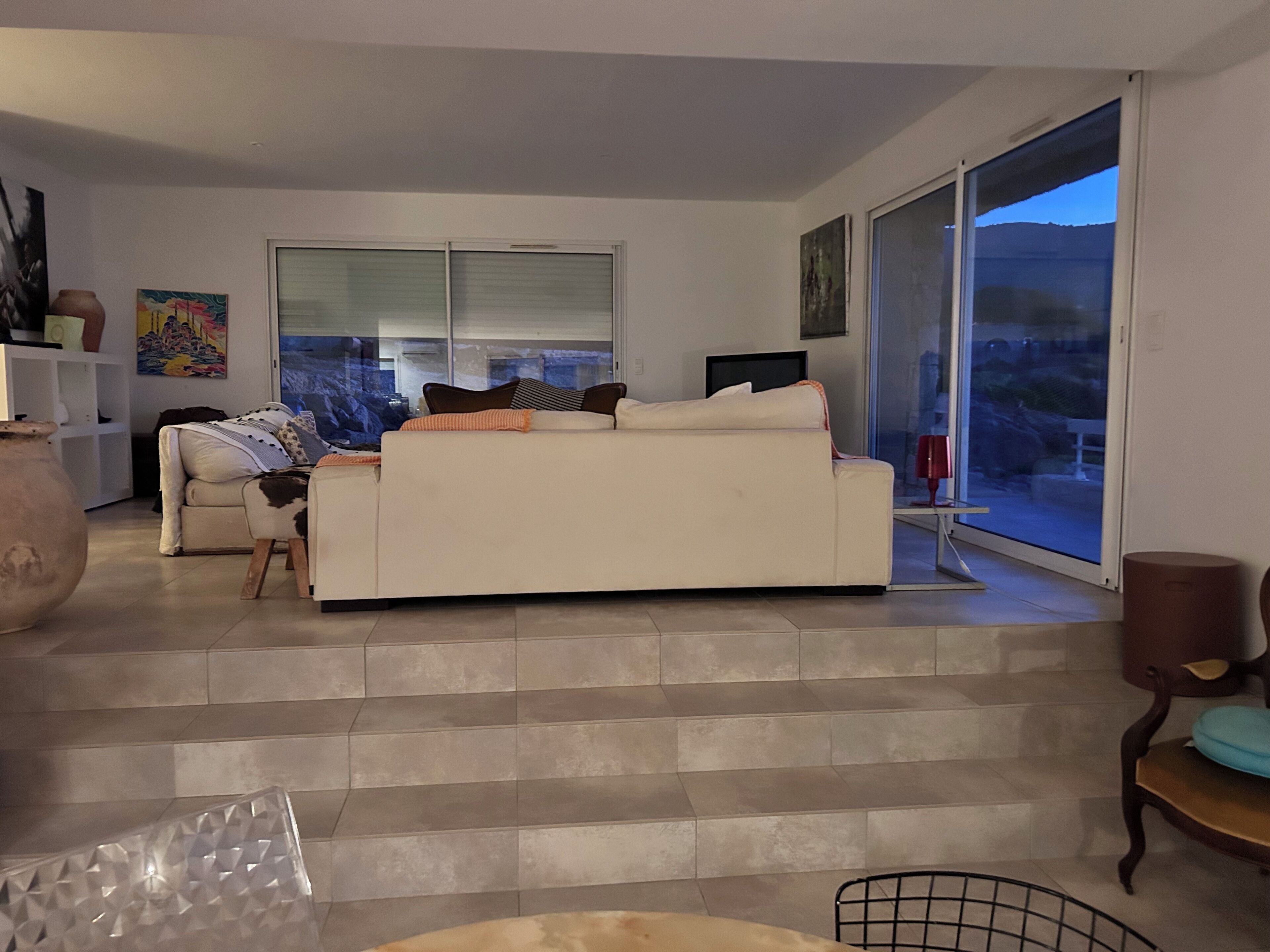 A living room with a sofa, a coffee table, and a TV. There are stairs leading to a balcony with a view.