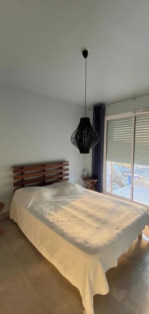 Ein Schlafzimmer mit einem großen Bett, einer Pendelleuchte und Blick durch ein Fenster.