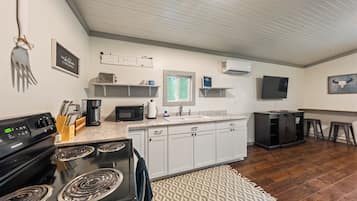 A kitchen with a stove, microwave, and coffee maker. There is a window with a view, a TV mounted on the wall, and a wooden floor.
