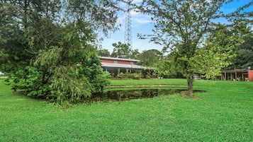 A grassy area with a pond, trees, and a building with a red roof.