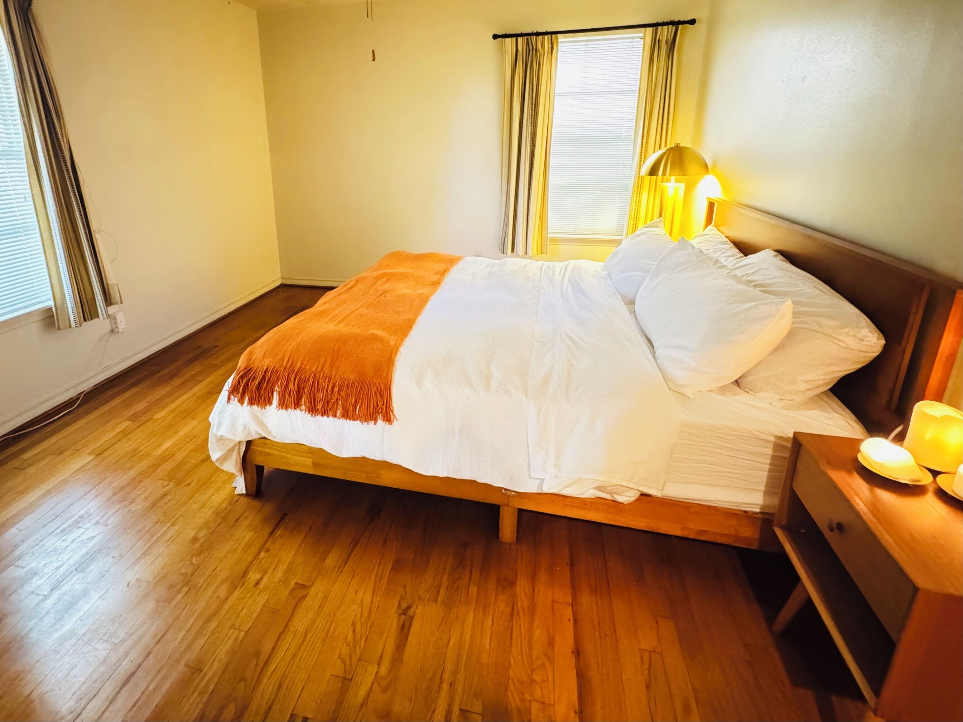 A bedroom with a wooden bed, a bedside table with a lamp, and a window with curtains.