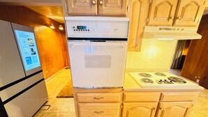 Una cocina compacta con horno y estufa integrados, armarios de madera y una pantalla digital en el refrigerador.