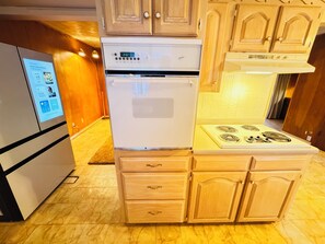 A compact kitchen with a built-in oven and stove, wooden cabinets, and a digital display on the refrigerator. - Vintage East Dallas 3 King Bed Retreat • Fire Pit • Grill Near White Rock Lake (Dallas)