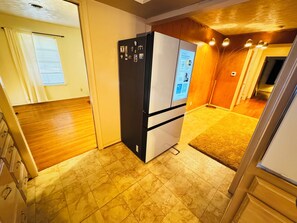 A compact kitchen with a refrigerator, wooden flooring, and a small window. - Vintage East Dallas 3 King Bed Retreat • Fire Pit • Grill Near White Rock Lake (Dallas)