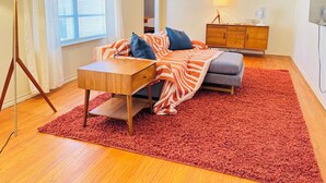 Un dormitorio acogedor con cama, una mesita, un tapete rojo y un armario de madera.