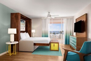 Habitación de hotel con cama, escritorio, silla, televisor y balcón con vistas.