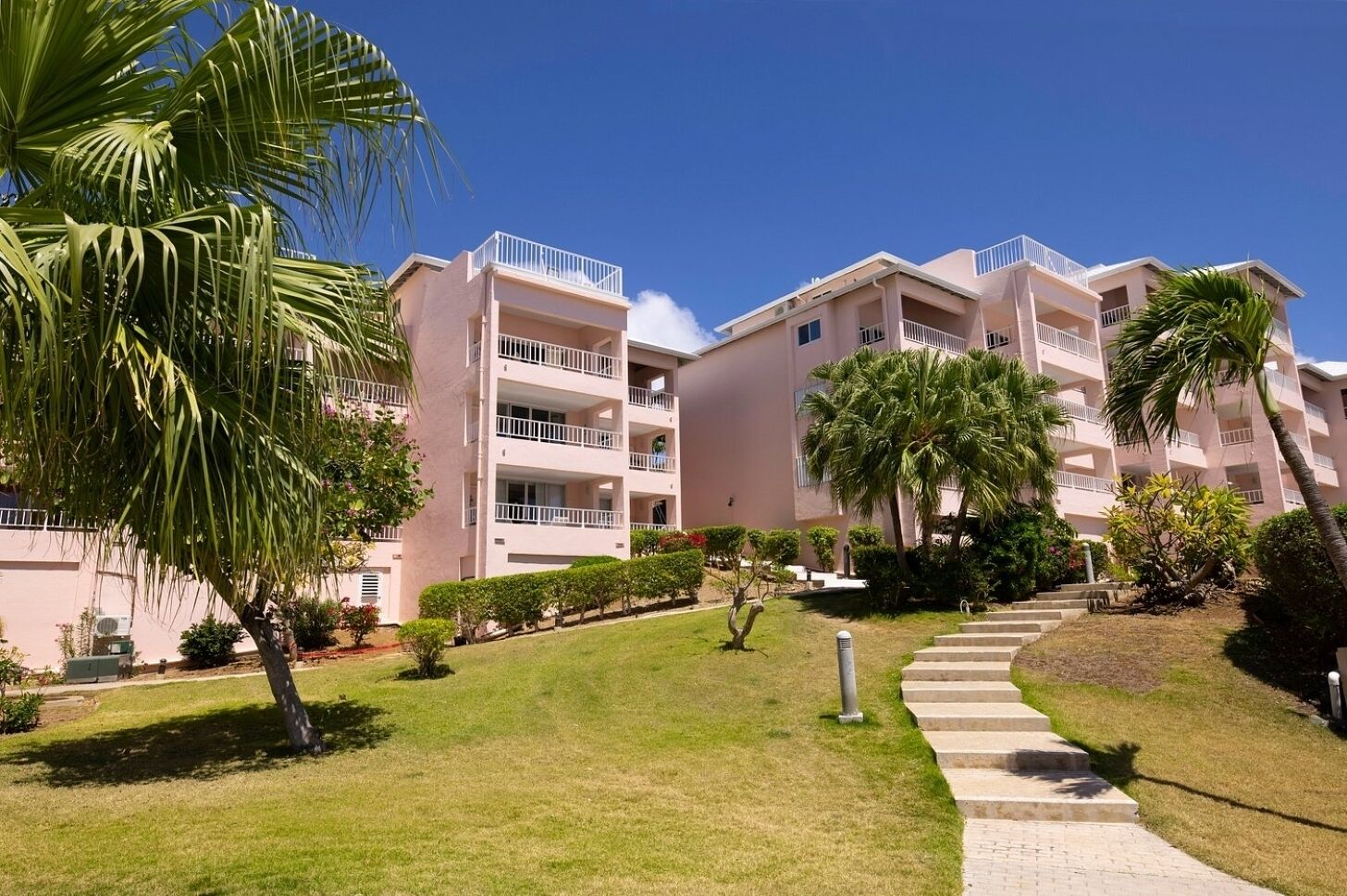 A multi-story hotel with balconies, a grassy lawn, and palm trees.