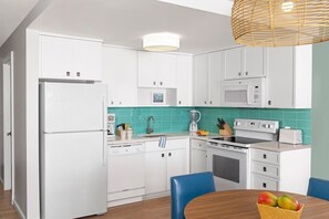 A modern kitchen with white cabinets, a microwave, a stove, and a sink. There is a dining table with chairs and a basket of fruit. - St. Thomas | Tropical Beach Retreat | Pool + Beach (St. Thomas)