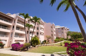 Un hotel de varios pisos con balcones, palmeras y jardines bien cuidados.