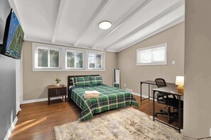 Een slaapkamer met een bed, een bureau, een stoel, een kastje en een raam.