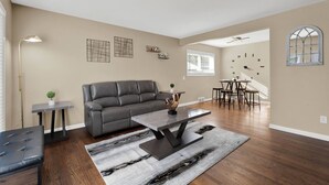 Uma sala de estar ampla com um sofá de couro cinza, uma mesa de centro e uma área de jantar com uma mesa redonda e cadeiras.
