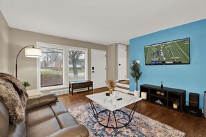 Ein Wohnzimmer mit einer Couch, einem Couchtisch, einem an der Wand montierten Fernseher und einer Bank.