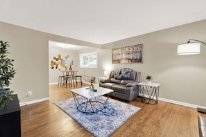 A living room with a sofa, coffee table, and a rug. There is a dining area in the background with a table and chairs. - 4BR Across 2 Adjacent Units - Downtown Birmingham (Birmingham)
