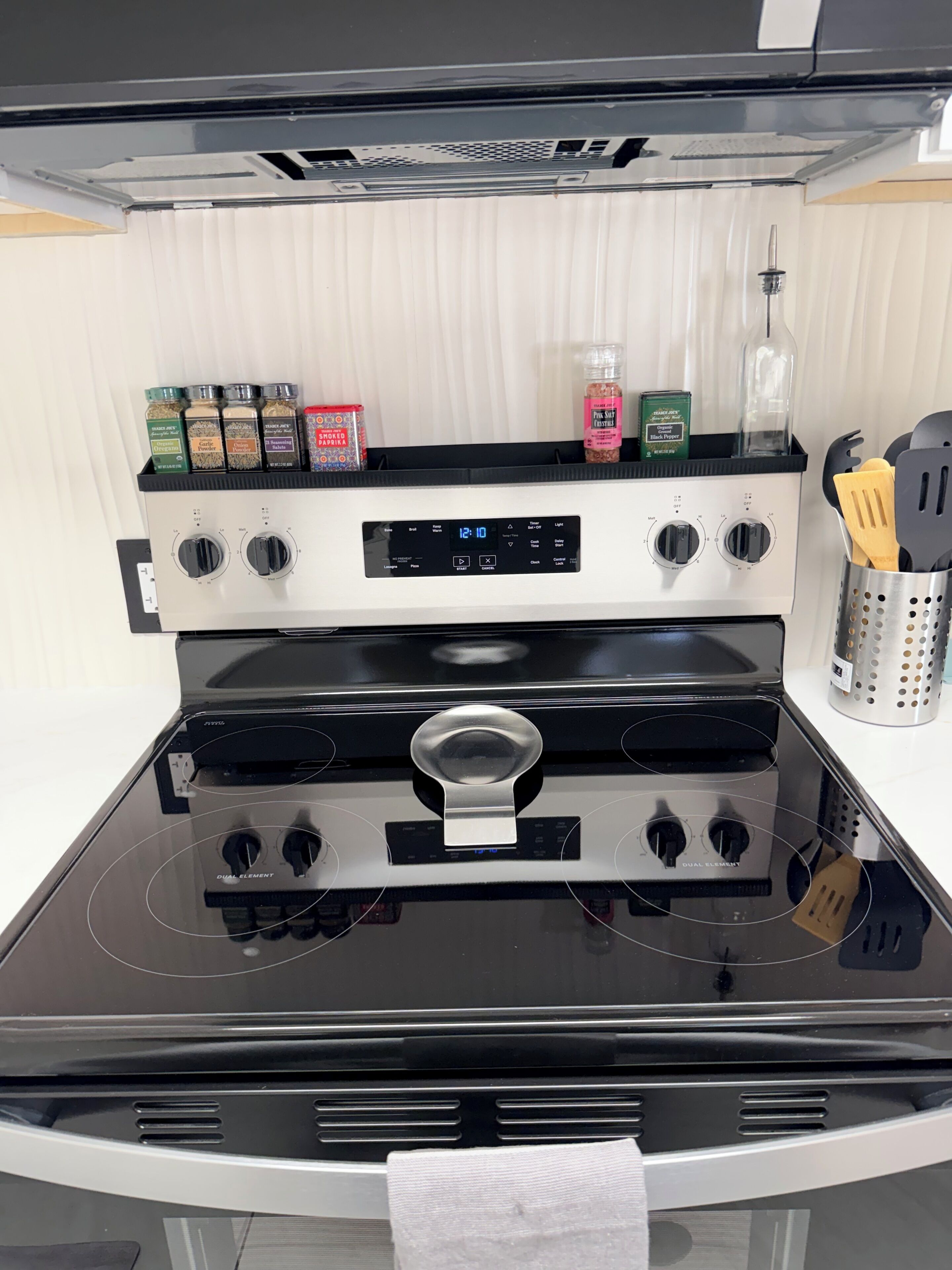 A kitchen with a black stove, a digital control panel, and various spices on the countertop.