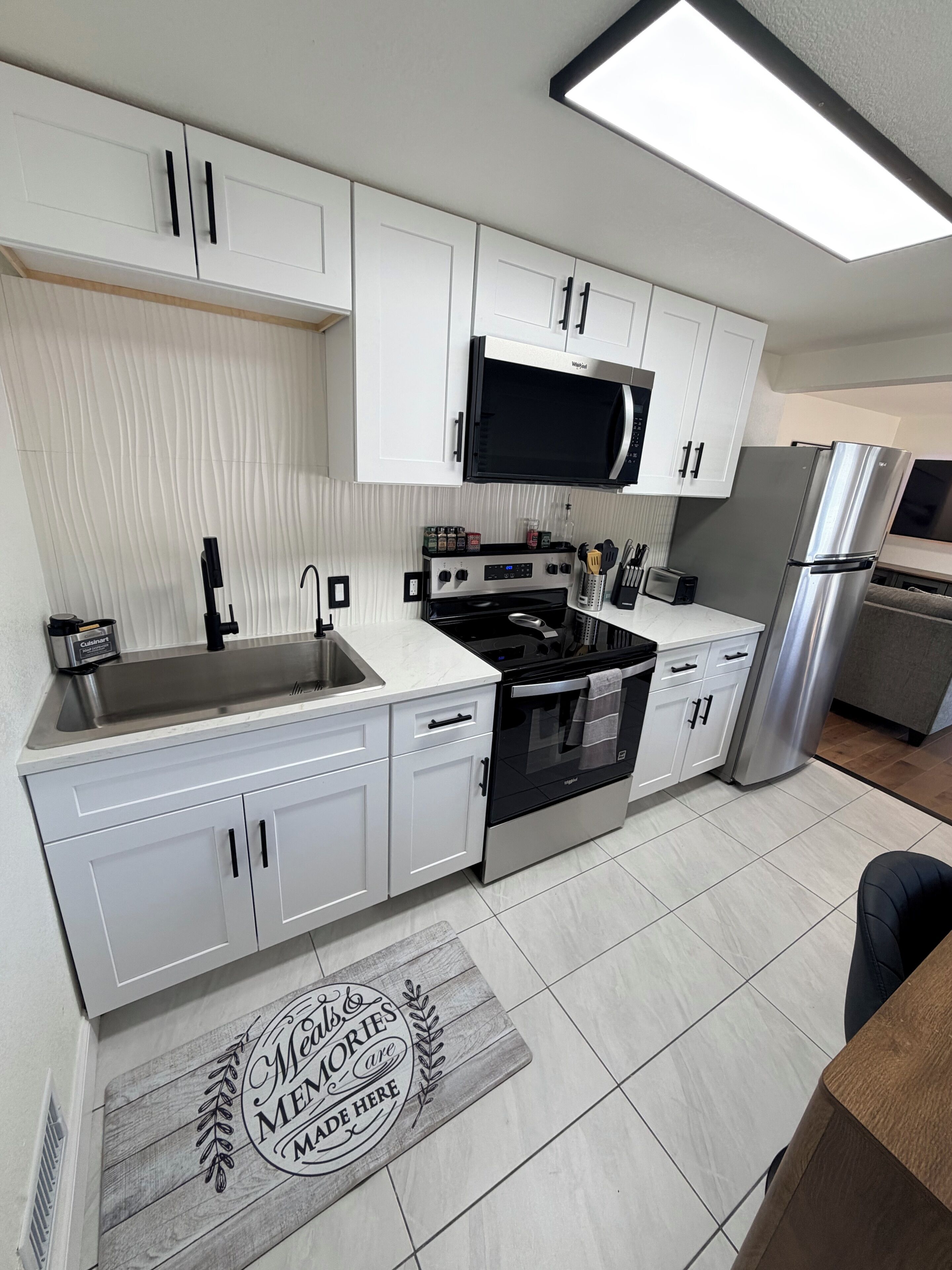 A modern kitchen with white cabinets, a stainless steel refrigerator, a microwave, and a stove.
