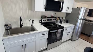 A modern kitchen with white cabinets, a stainless steel refrigerator, a microwave, and a stove.