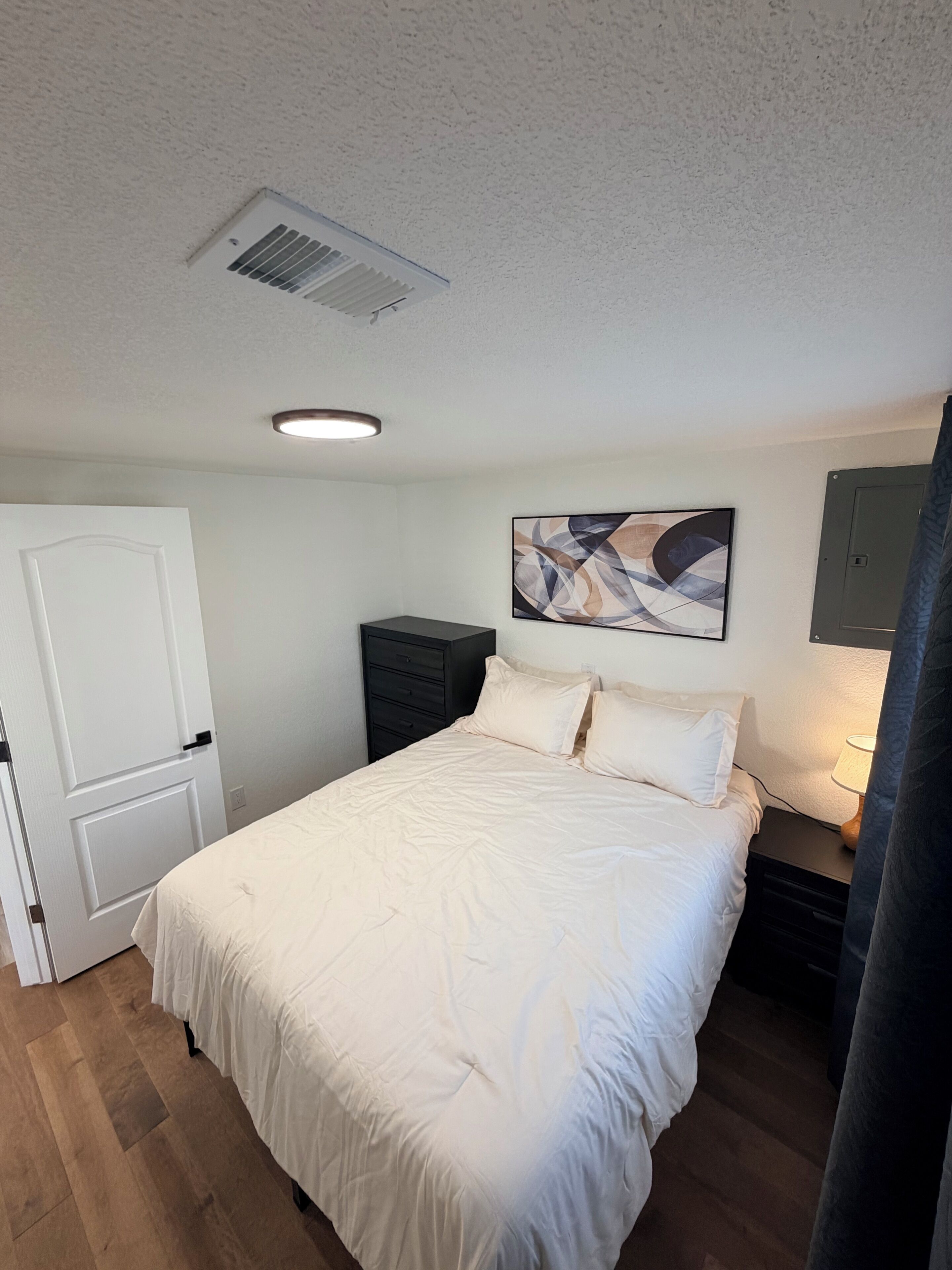 Une chambre à coucher comprenant un lit, une table de chevet, une œuvre d’art accrochée au mur et une porte.