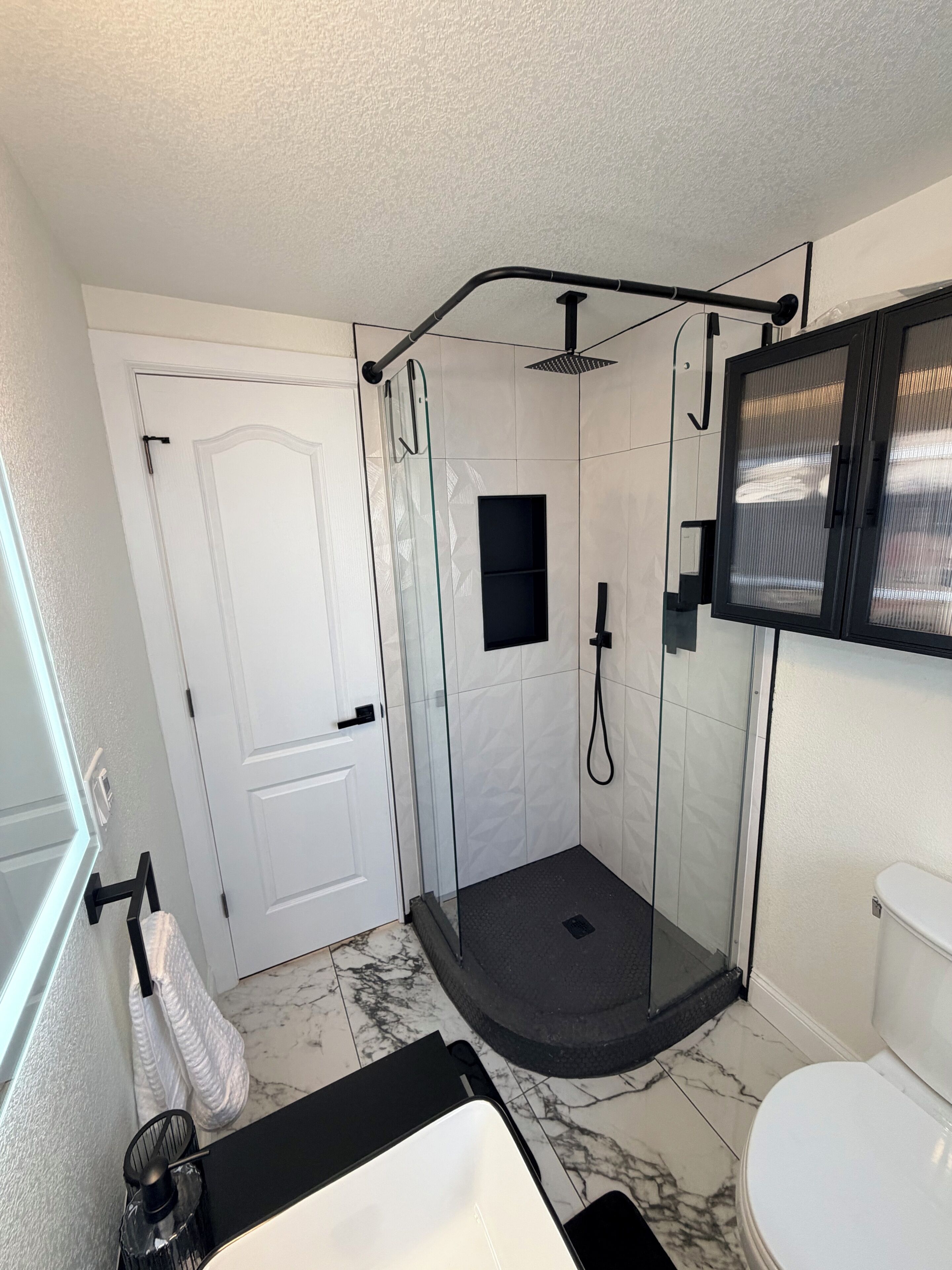 Ein Badezimmer mit einer gläsernen Duschkabine, einer weißen Toilette und einem schwarzen Waschbecken.