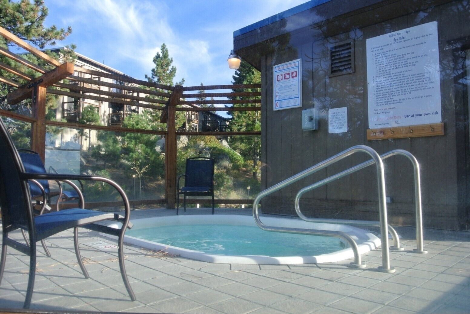An outdoor swimming pool with a wooden pergola, a chair, and a signboard with spa rules.