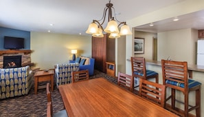 A dining area with a wooden table and chairs, a sofa with patterned upholstery, a fireplace, and a television mounted on the wall.
