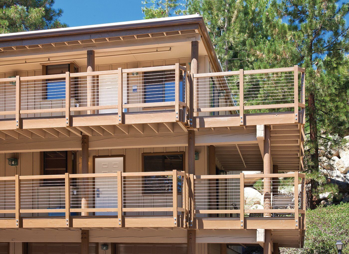 A multi-story wooden building with balconies, a garage, and a stone wall.