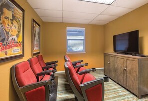 A room with three red cinema-style chairs, a television on a wooden cabinet, and a window with blinds.