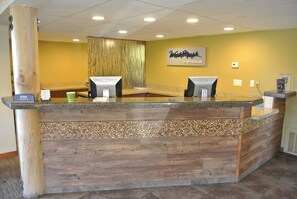 A reception desk with a wooden design, two computer monitors, and a sign that reads "Welcome Mark by Wyndham".