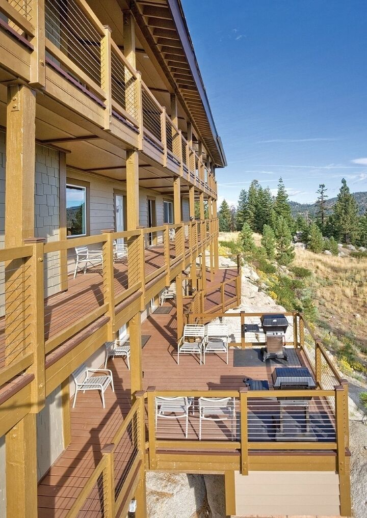 A multi-story wooden building with balconies, outdoor seating, and a view of a forested landscape.
