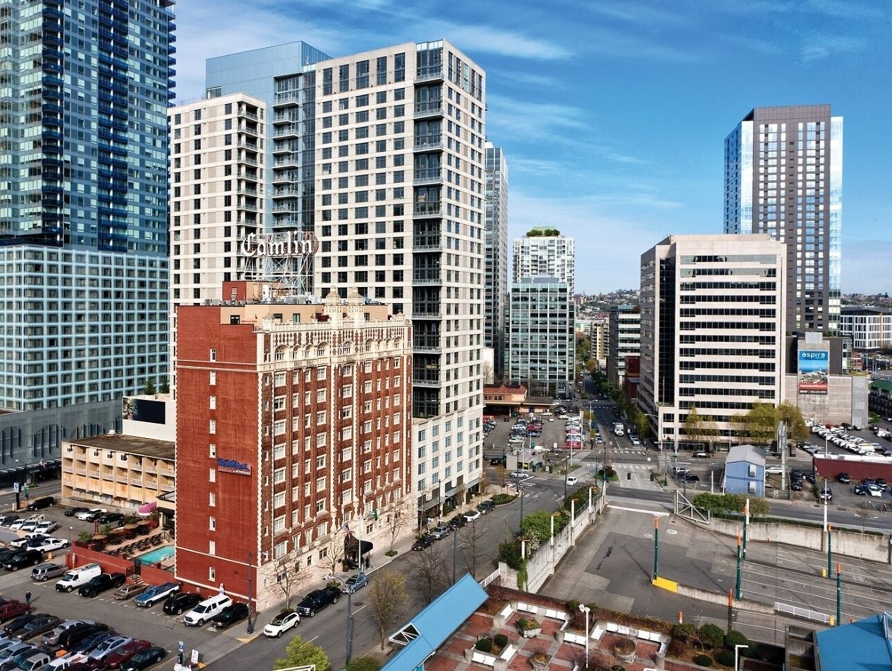 A high-rise building with a grid of windows, surrounded by other tall buildings and a parking lot.