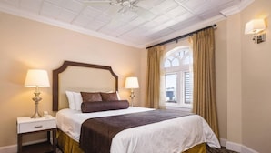 Una habitación de hotel con una cama grande, dos mesitas de noche con lámparas, una ventana con cortinas y una alfombra estampada.