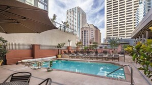 Una piscina exterior con sillones de descanso y sombrillas, rodeada por un complejo de edificios altos.