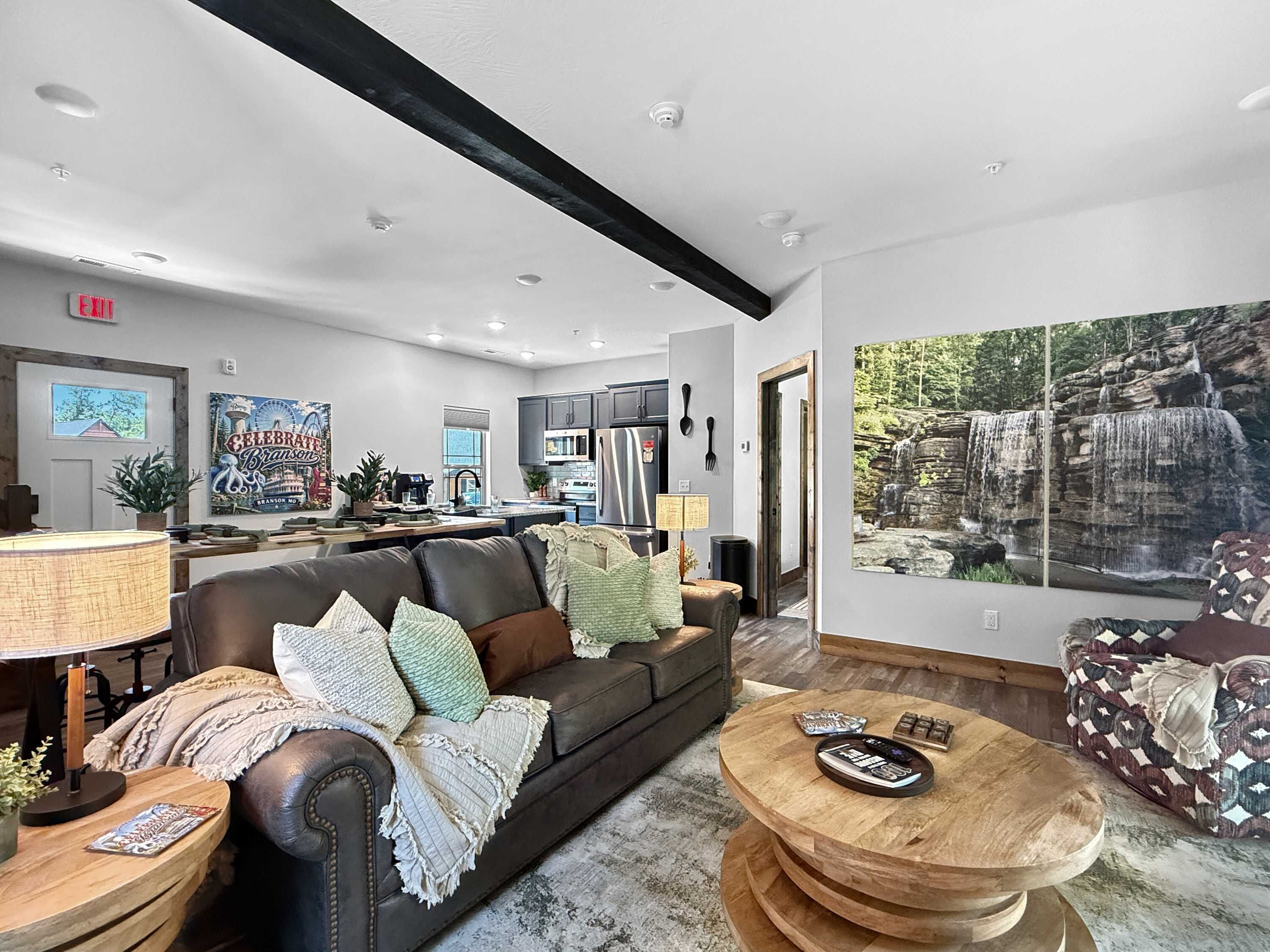 A modern living room with a leather sofa, a round wooden coffee table, and a large painting of a waterfall.