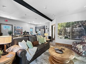 A modern living room with a leather sofa, a round wooden coffee table, and a large painting of a waterfall.