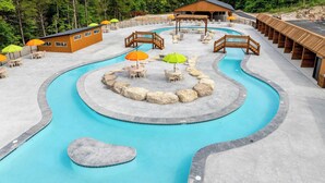 A pool area with wooden structures, lounge chairs, and umbrellas.