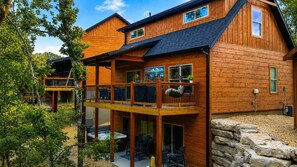 A two-story wooden cabin with a balcony, a hot tub, and a stone wall.