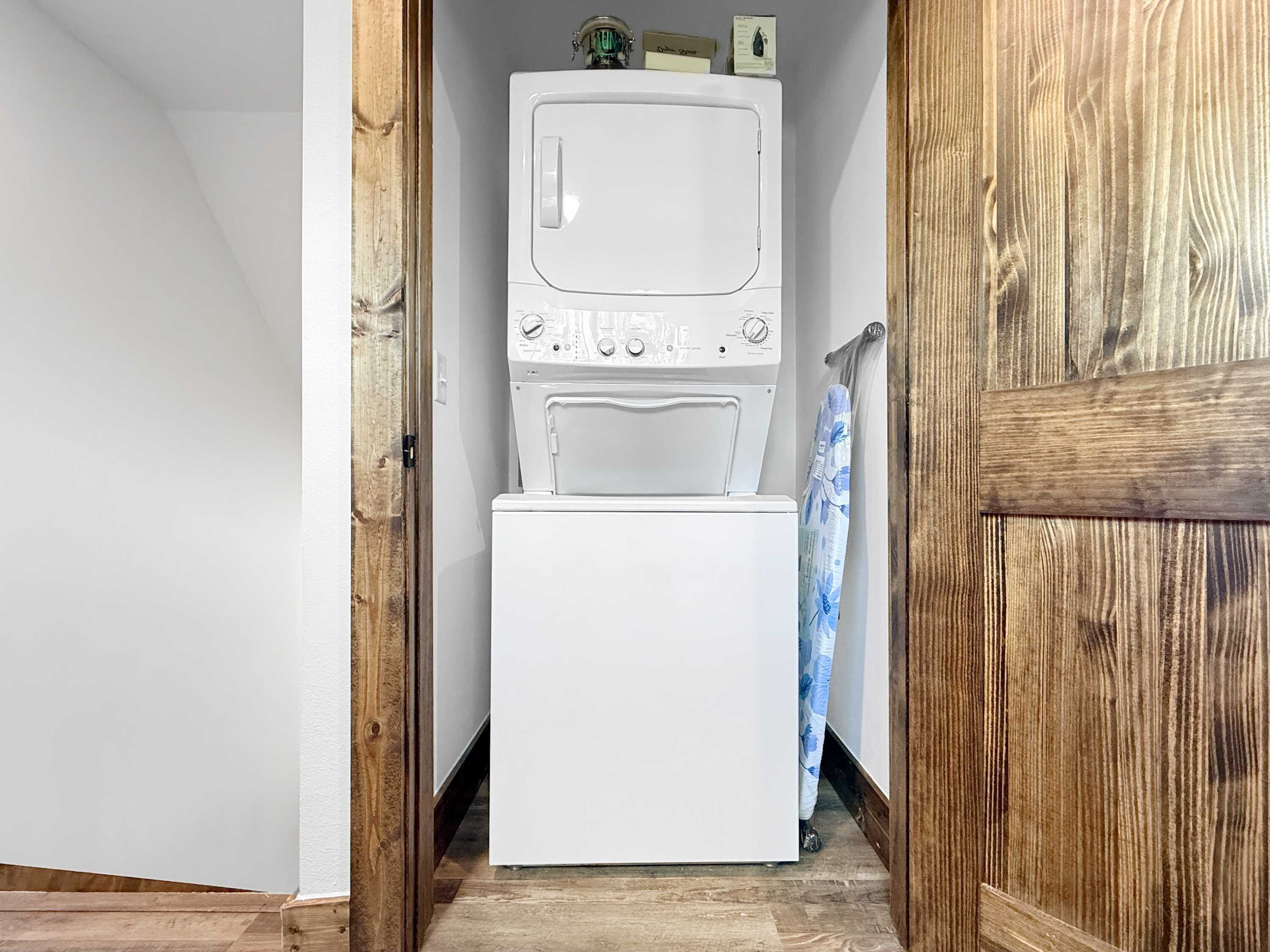 A laundry area with a stacked washer and dryer, wooden flooring, and a door leading to another room.