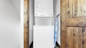 A laundry area with a stacked washer and dryer, wooden flooring, and a door leading to another room.