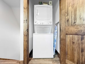 A laundry area with a stacked washer and dryer, wooden flooring, and a door leading to another room.