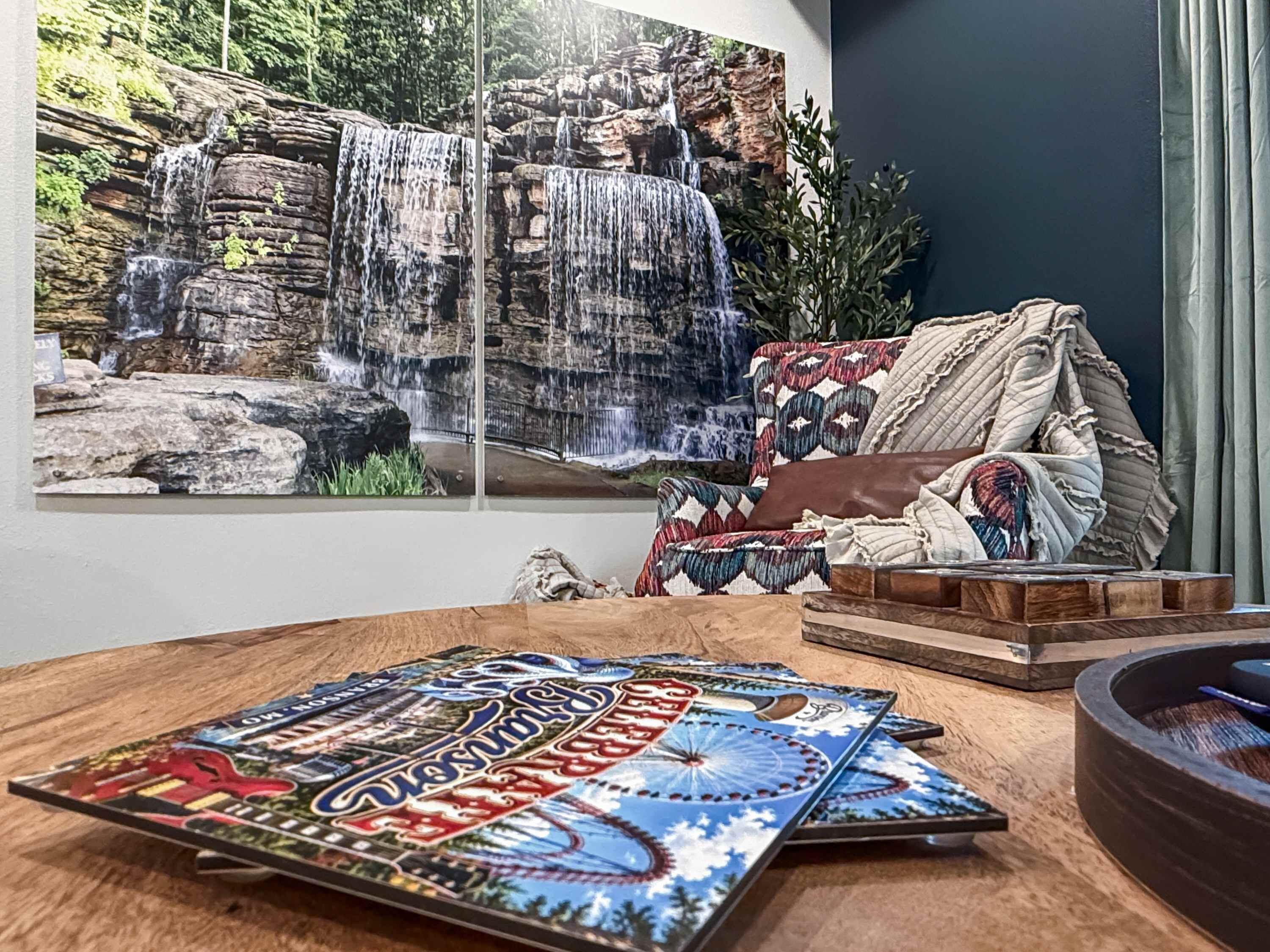 Une pièce décorée d’une grande fresque représentant une cascade, d’un canapé à motifs et d’une table en bois agrémentée d’un objet décoratif.