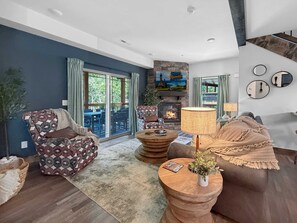 A modern living room with a fireplace, a dining area with outdoor access, and a large window.