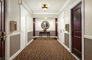 A hallway with patterned carpet, a mirror, and a table with flowers.