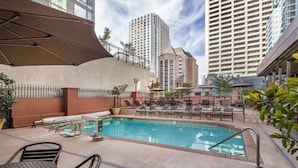 An outdoor swimming pool with lounge chairs and umbrellas, surrounded by a high-rise building complex.