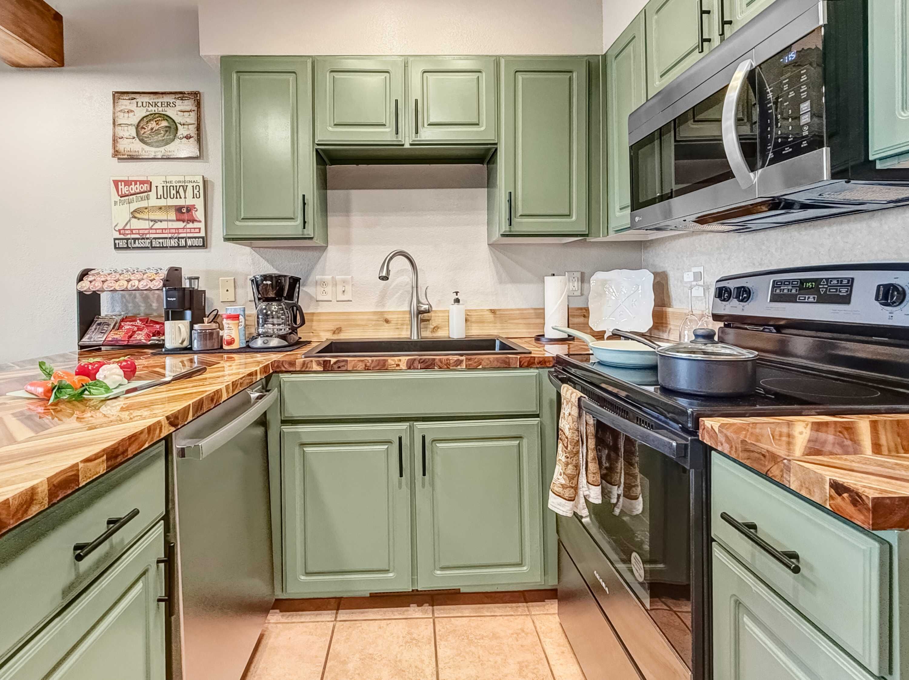 A kitchen with green cabinets, a microwave, a stove, and a coffee maker.