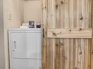 Une petite buanderie blanche, avec une porte en bois et une petite étagère où sont posés quelques articles.