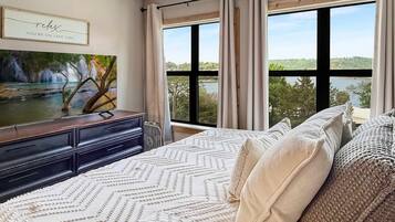 Ein Schlafzimmer mit Bett, Schminktisch, einem Gemälde und einem Fenster mit Blick auf einen See und Bäume.