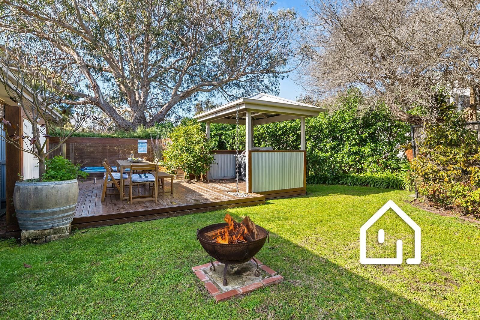 A backyard with a fire pit, a covered patio, and a wooden deck.