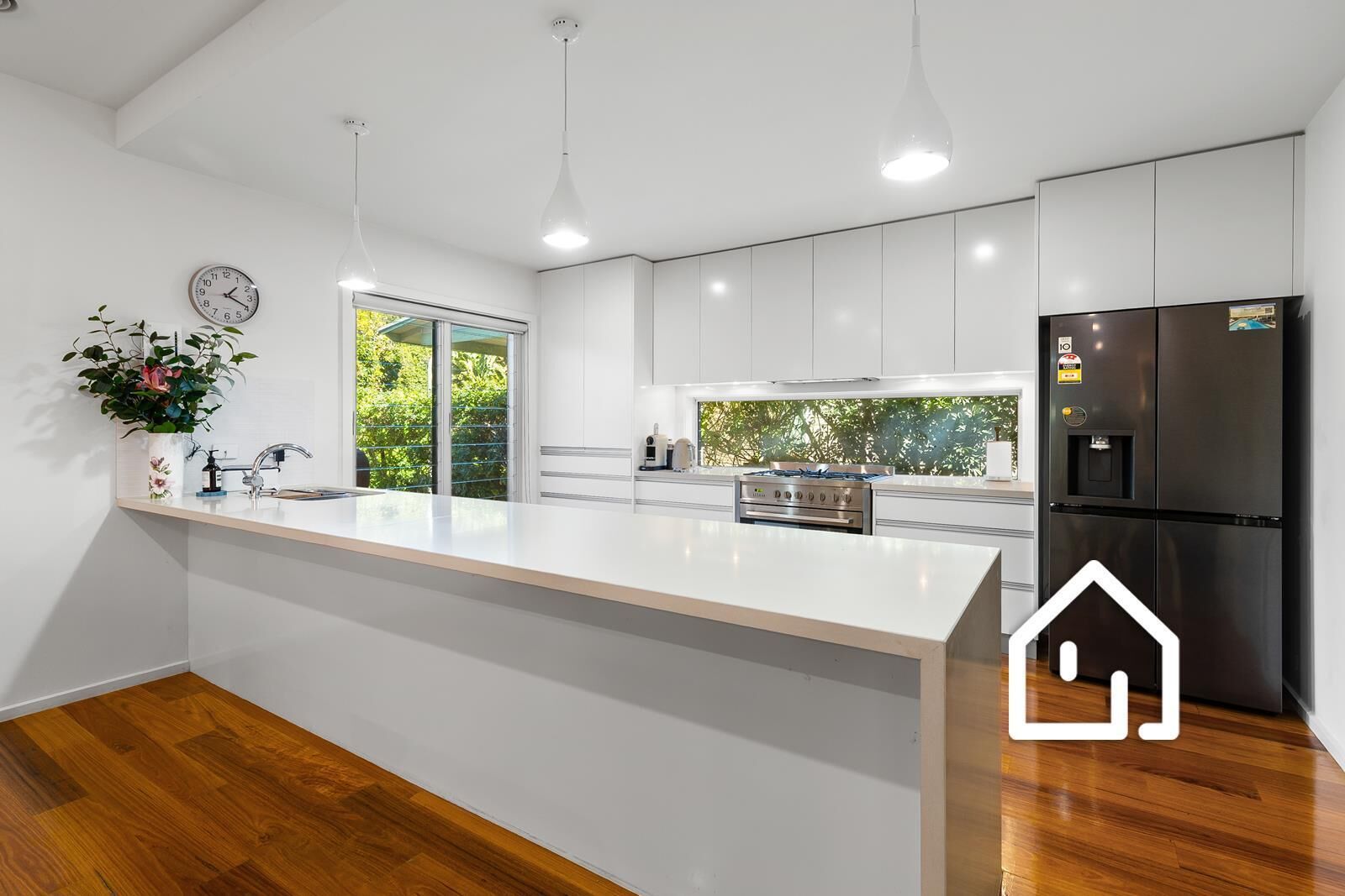 Een moderne keuken met een centraal eiland, roestvrijstalen apparatuur en uitzicht op groen.