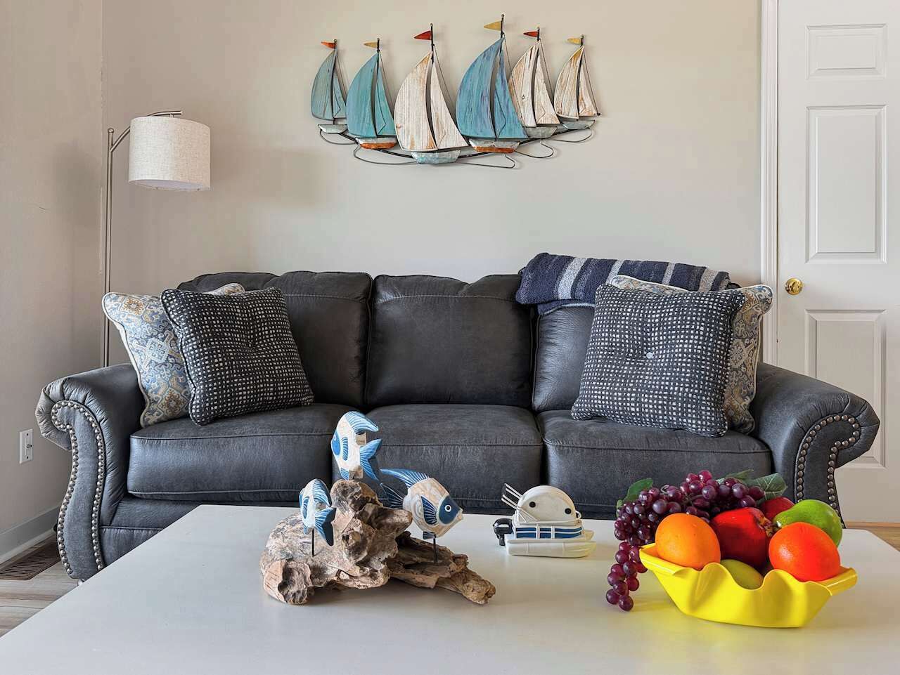 Een woonkamer met een donker leren bank, decoratieve wandkunst, een witte salontafel en een fruitschaal.